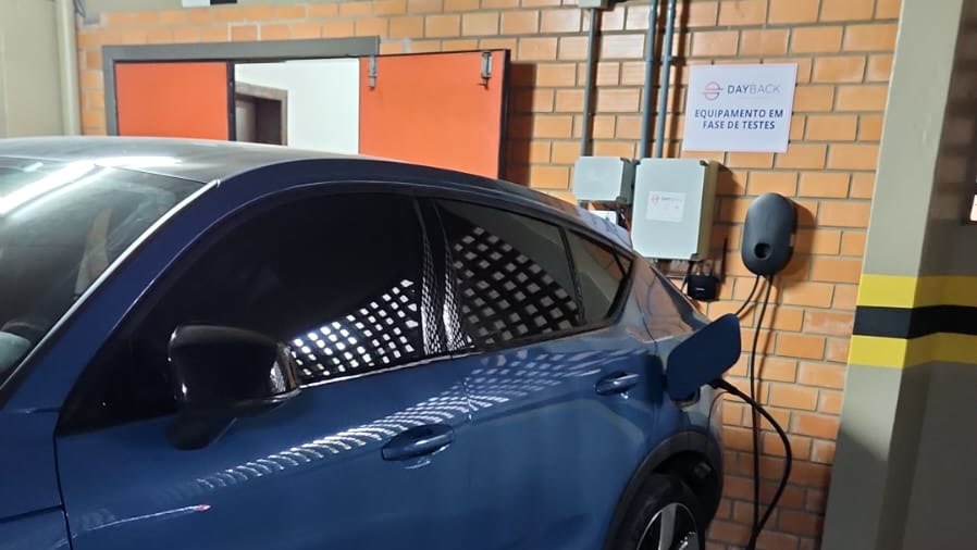 Veículo elétrico azul recarregando no primeiro ponto DayBack Charger, ao lado da placa Equipamento em fase de testes